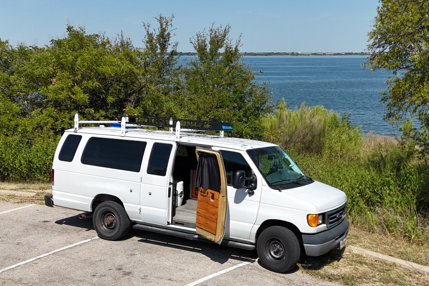 White converted van, perfect for an RV rental adventure, parked lakeside with its side door open showing a cozy interior.