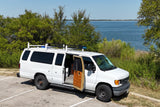 White converted van, perfect for an RV rental adventure, parked lakeside with its side door open showing a cozy interior.