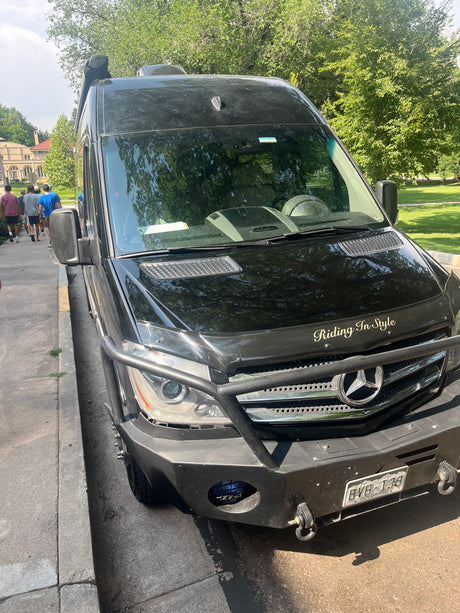 Front of a custom black Mercedes Sprinter, an RV rental, with a heavy-duty bumper & "Riding In Style" text.