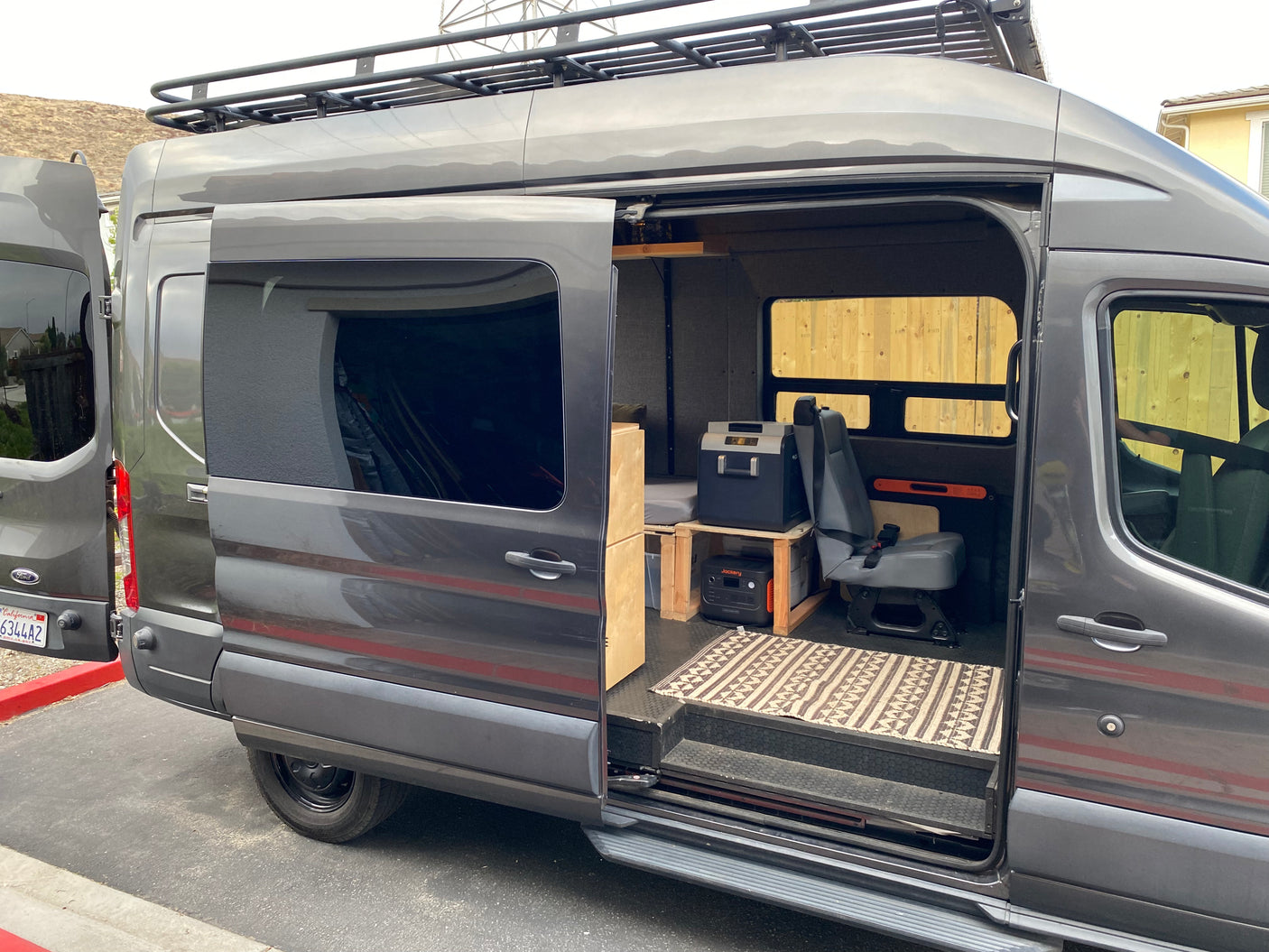 Explore this grey RV rental camper van! Its open side door reveals a custom interior with bed, fridge, and power station.