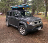 Grey Honda Element with paddleboards, parked at a wooded campground. A great alternative to an RV rental.