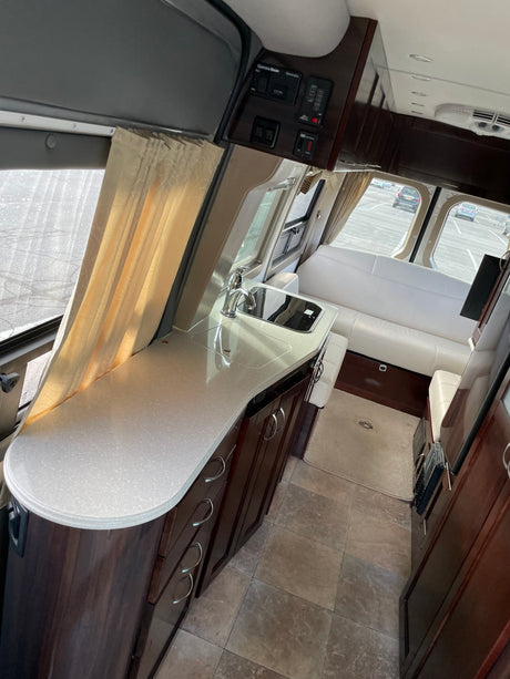 Inside a premium RV rental: kitchenette with sink, elegant wood cabinets, and rear sofa seating. Ideal for travel.