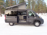 This gray Tofino pop-top camper van, an ideal rv rental, is parked in a snowy forest with its side door open.