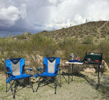 RV rental adventure: two blue camping chairs and a portable kitchen set up in a desert landscape with saguaro cacti under a cloudy sky.