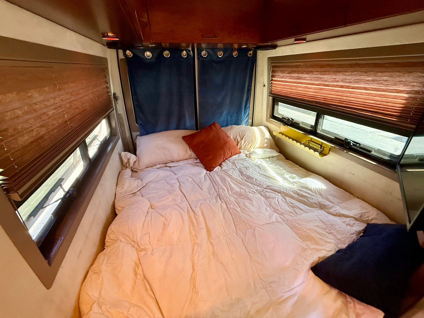 Experience comfort in this rv rental bedroom featuring a bed, warm comforter, pillows, side windows with blinds, and privacy curtains.