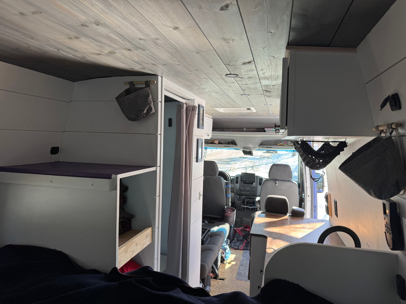 Custom van conversion RV rental interior. From bed, see wood-paneled ceiling, white storage units, and driver's cabin. — photo 8