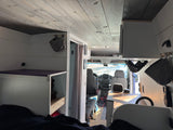 Custom van conversion RV rental interior. From bed, see wood-paneled ceiling, white storage units, and driver's cabin.