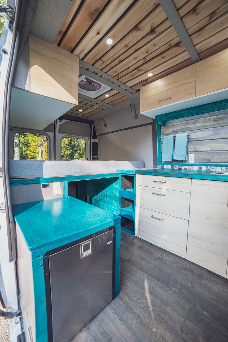 Explore in comfort with this RV rental! Van interior features a modern kitchen with teal and wood, cozy bed, and wooden ceiling. — photo 7