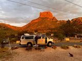 Stunning RV rental camping adventure! White campervan with awning at a scenic desert mountain campsite at sunset.