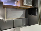 Cozy RV rental interior with light gray dinette, window blinds, TV, and AC for comfort. Perfect for your next adventure.