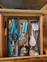 Neatly organized RV rental kitchen drawer with spatulas, can opener, measuring cups, and shears.