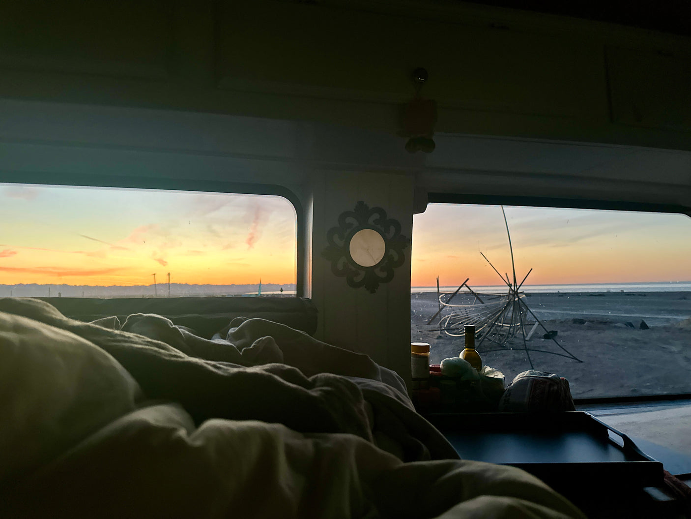 Cozy RV rental bedroom view: serene sunrise over beach, mountains, and unique outdoor structures. A perfect travel morning.