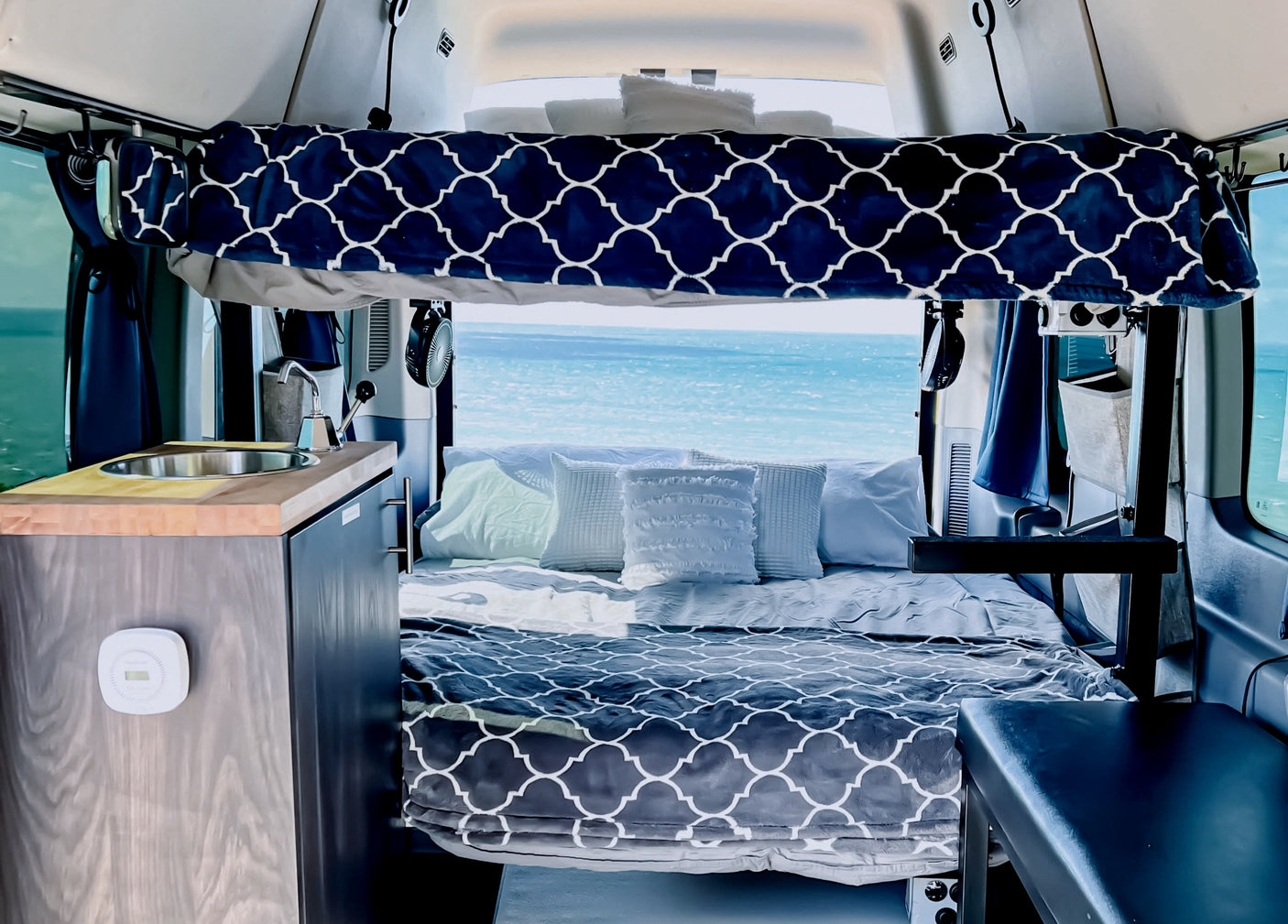 Cozy RV rental interior with a comfortable bed, kitchenette, and stunning ocean view, ideal for adventurous travel.