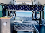 Cozy RV rental interior with a comfortable bed, kitchenette, and stunning ocean view, ideal for adventurous travel.