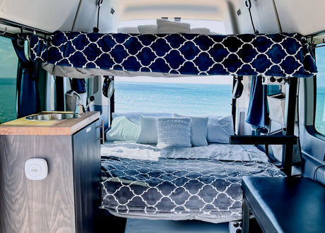 Cozy RV rental interior with a comfortable bed, kitchenette, and stunning ocean view, ideal for adventurous travel.