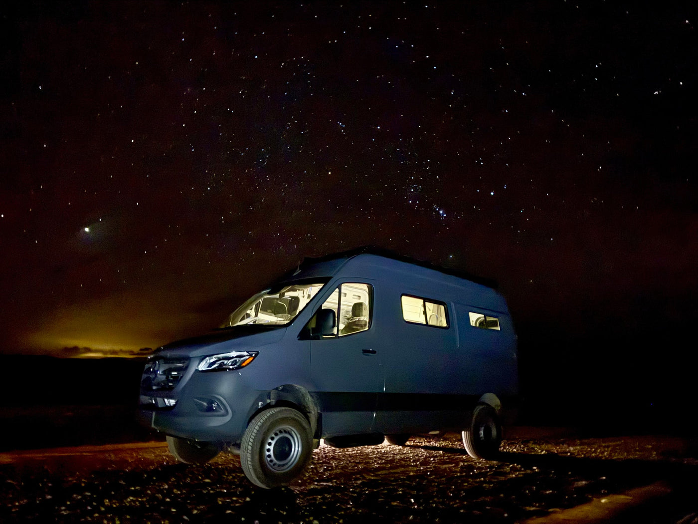 RV rental: Dark Mercedes Sprinter camper van, lights aglow, parked under a brilliant starry night sky for van life adventures. — photo 6
