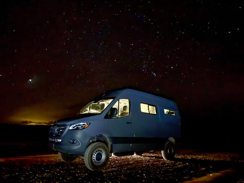 RV rental: Dark Mercedes Sprinter camper van, lights aglow, parked under a brilliant starry night sky for van life adventures. — photo 6