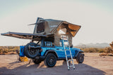 Blue Jeep with a rooftop tent and awning set up in the desert, offering a unique camping experience. Consider for your rv rental.