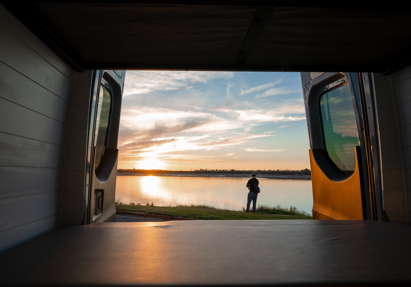 Perfect RV rental evening: open van doors reveal a tranquil sunset over water, with a person enjoying the view.