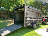This grey adventure rv rental trailer has an open ramp door, fold-up bed inside, Thule awning, & rugged tires.