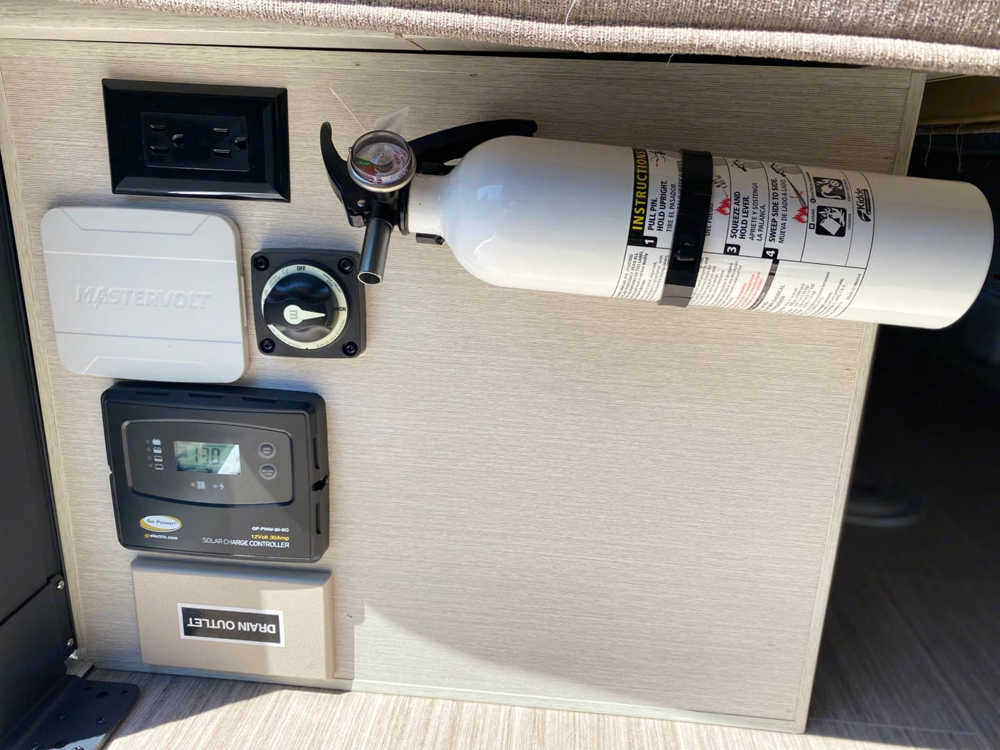 An rv rental's power panel: solar charge controller, AC outlet, battery switch, and fire extinguisher for safety.