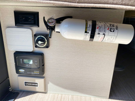 An rv rental's power panel: solar charge controller, AC outlet, battery switch, and fire extinguisher for safety.