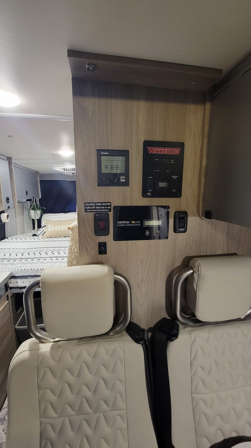 RV rental interior shows main control panel for power, water, & heating, with solar charge display. Beige seats ready for travel. — photo 8