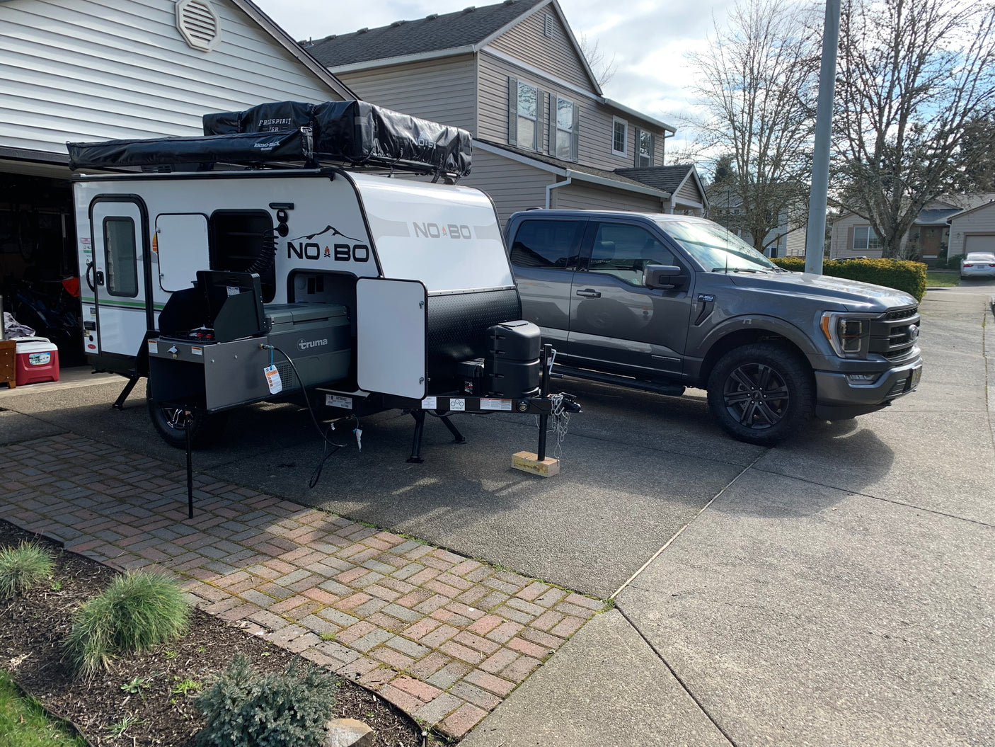 An RV rental: a gray F-150 truck towing a white NO BO camper with a rooftop tent and outdoor kitchen setup.