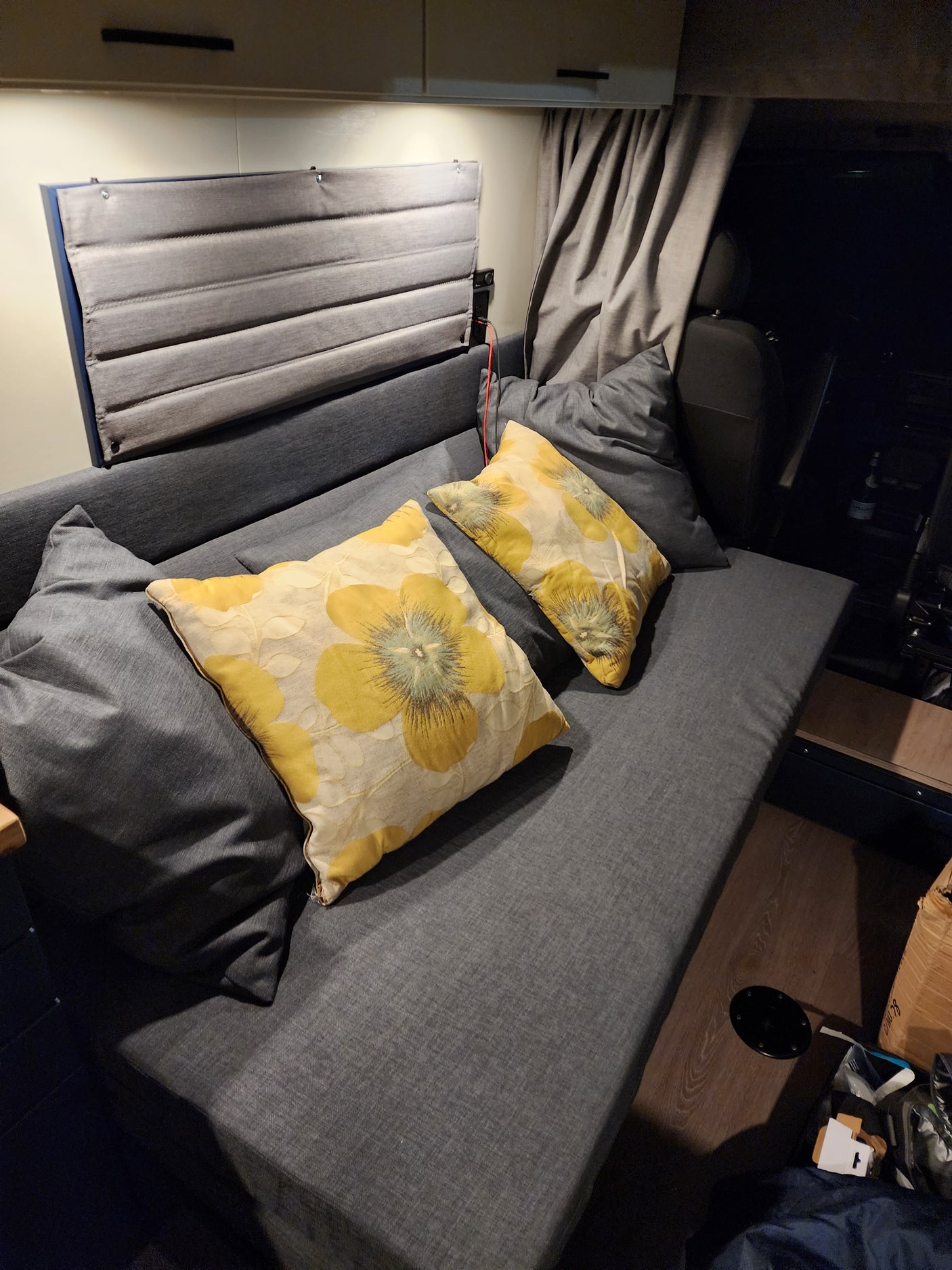 Inside an RV rental: a comfortable grey sofa with two yellow floral cushions and pleated window blinds.