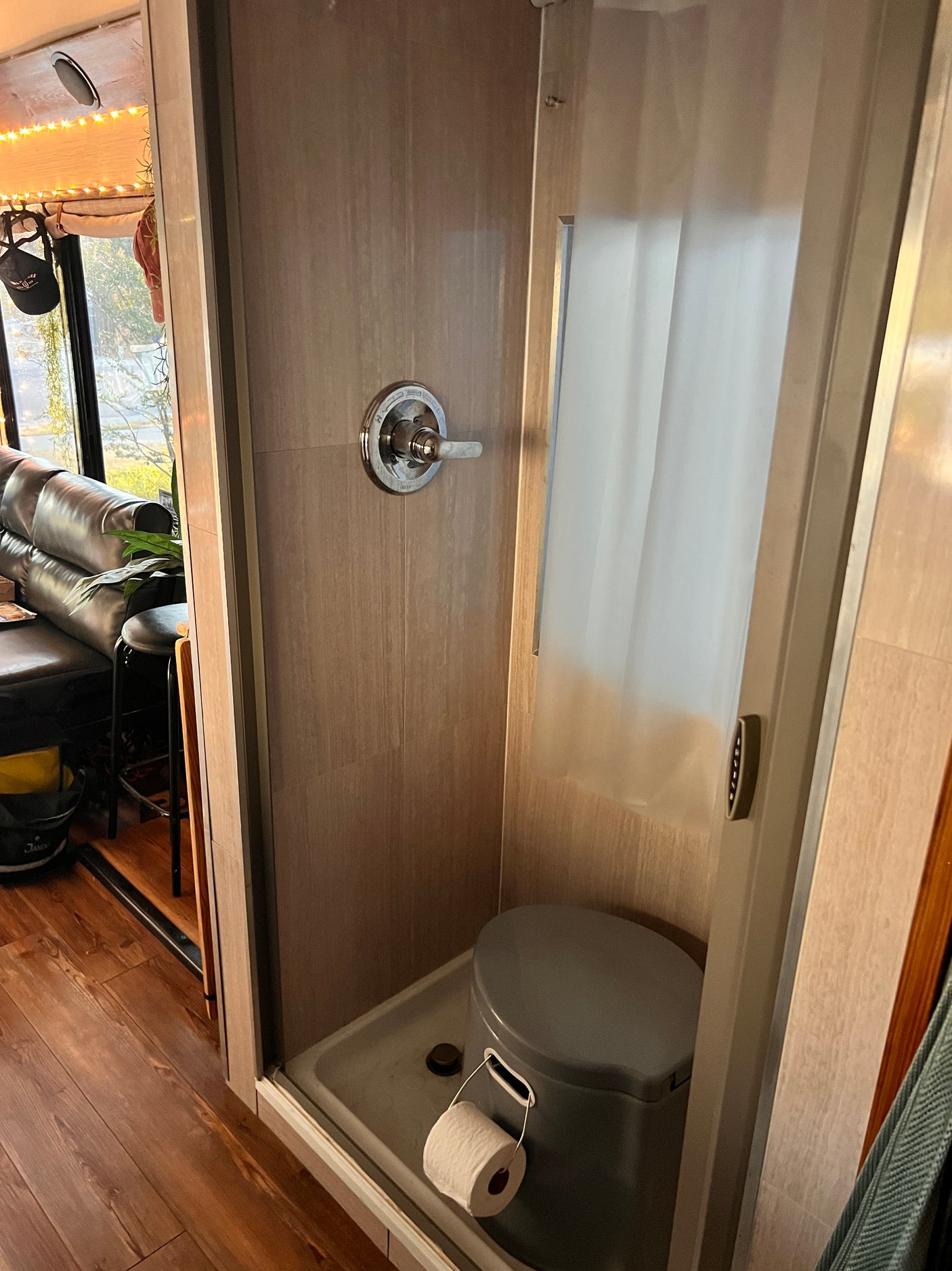 Inside an RV rental: a compact bathroom featuring a shower with controls, a portable toilet, and a roll of toilet paper.