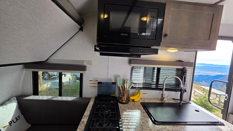 Cozy RV rental interior: kitchen with microwave, stove, sink, dining bench, and scenic mountain views outside. — photo 18