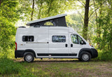 White Solis camper van with raised pop-top roof, parked on grass in a wooded setting. Ideal for rv rental adventures.