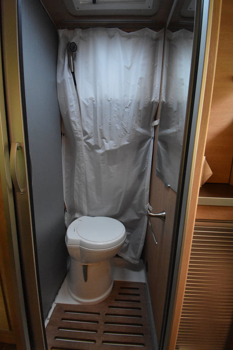 Compact RV rental bathroom: integrated toilet and shower with curtain, perfect for road trips.