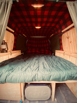 Experience comfort in this **rv rental**! Features a cozy red plaid interior, full bed, wood trim, and cooler storage.