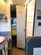 This RV rental interior shows a compact kitchen, an open bathroom/shower with controls, and a cozy sleeping area beyond.