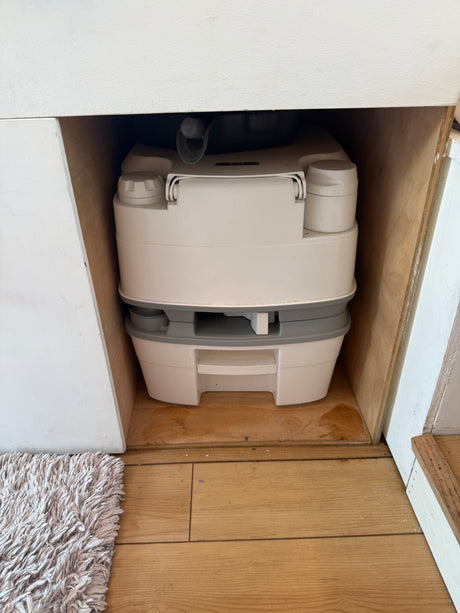 A light-colored Thetford portable chemical toilet stored in a wooden compartment, essential for any RV rental adventure.