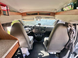 RV rental interior showing driver's cab, steering wheel, seats, dashboard, and overhead storage with a first aid kit.