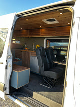 RV rental: Inside a modern camper van with wooden ceiling, equipped kitchen, captain's chairs, and rear bed for adventure.