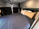 This RV rental's interior features a cozy bed with pillows, window coverings, and overhead storage.