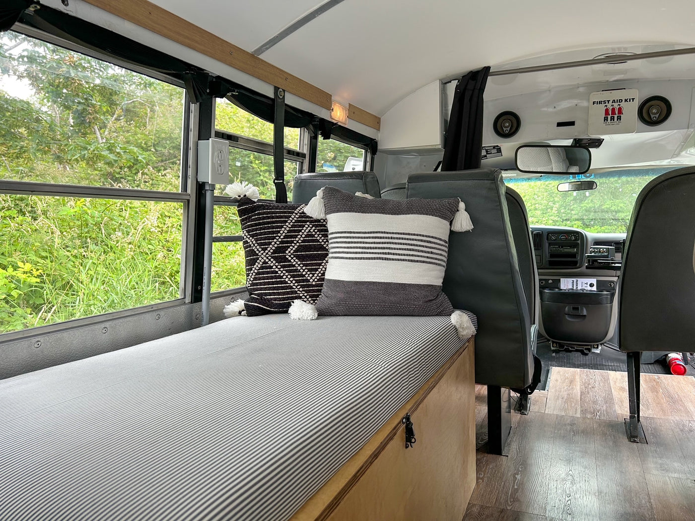 Experience our RV rental: a spacious bus camper with a cozy striped bed, decorative pillows, and nature views. — photo 7