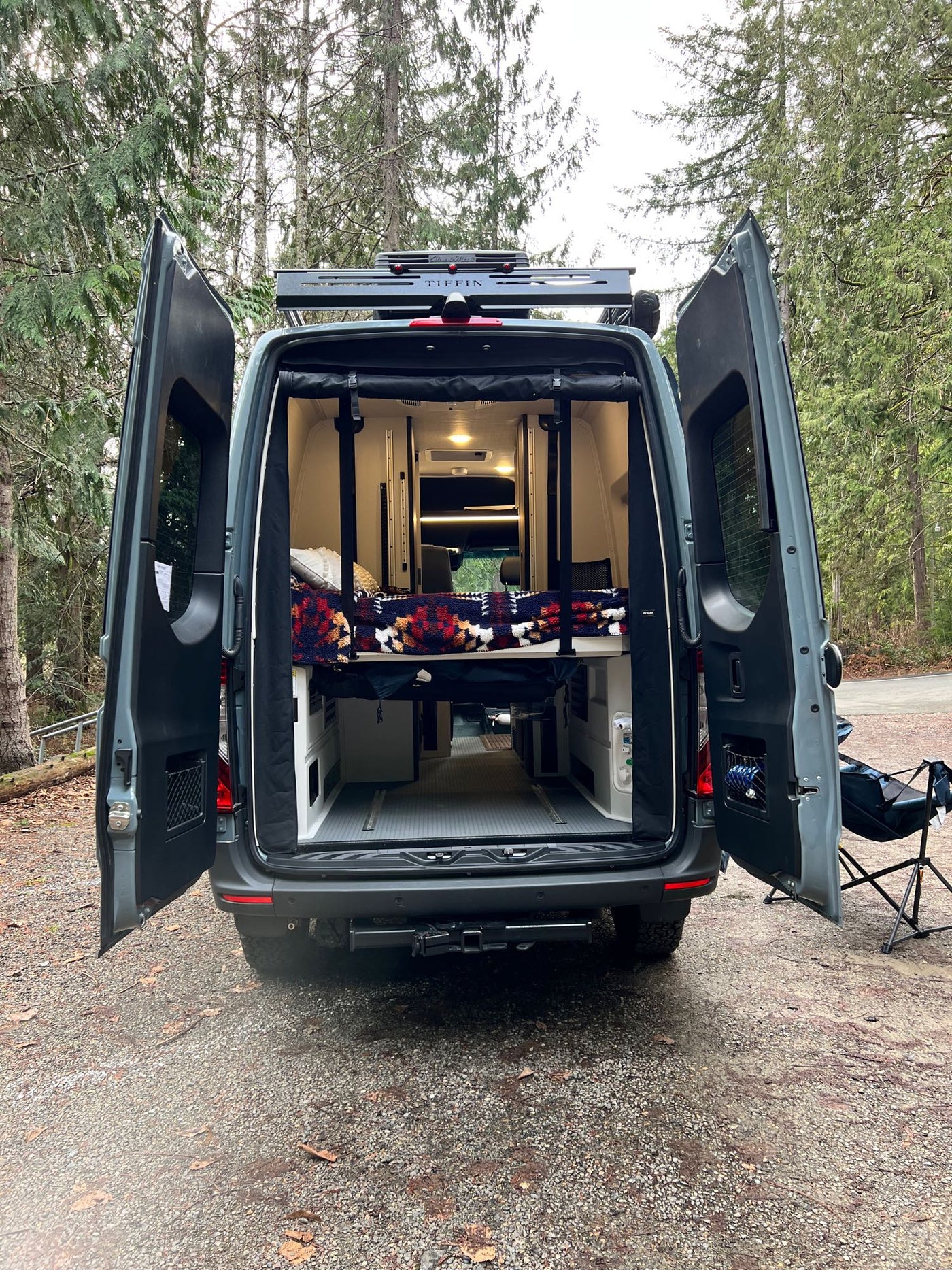  is set up at a campsite with its awning extended and dogs relaxing.|This RV rental camper van floor plan details the interior: rear power lift bed with gear garage — photo 11