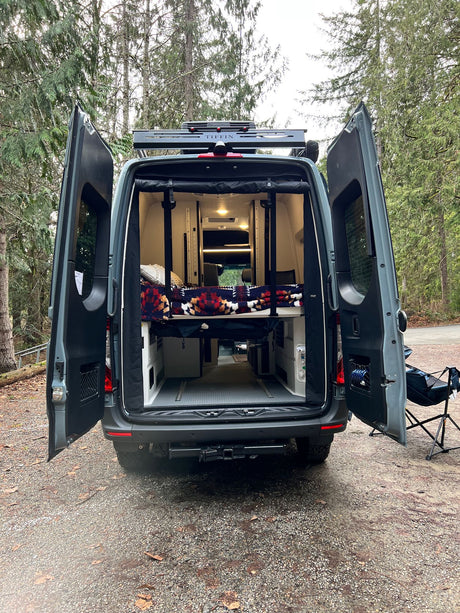 Open doors of a Tiffin camper van reveal its cozy interior, ready for your next rv rental adventure in the woods.
