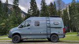 A grey Winnebago Revel 4x4 camper van, perfect for rv rental mountain adventures, amidst tall pines.