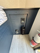 Inside an RV rental bedroom nook: includes a GFCI outlet, CO detector, speaker, and fire extinguisher by light wood flooring.