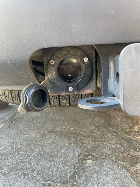 Close-up of an RV rental's rear bumper, featuring a 120V electrical outlet and tow hitch. Connect for auxiliary power.