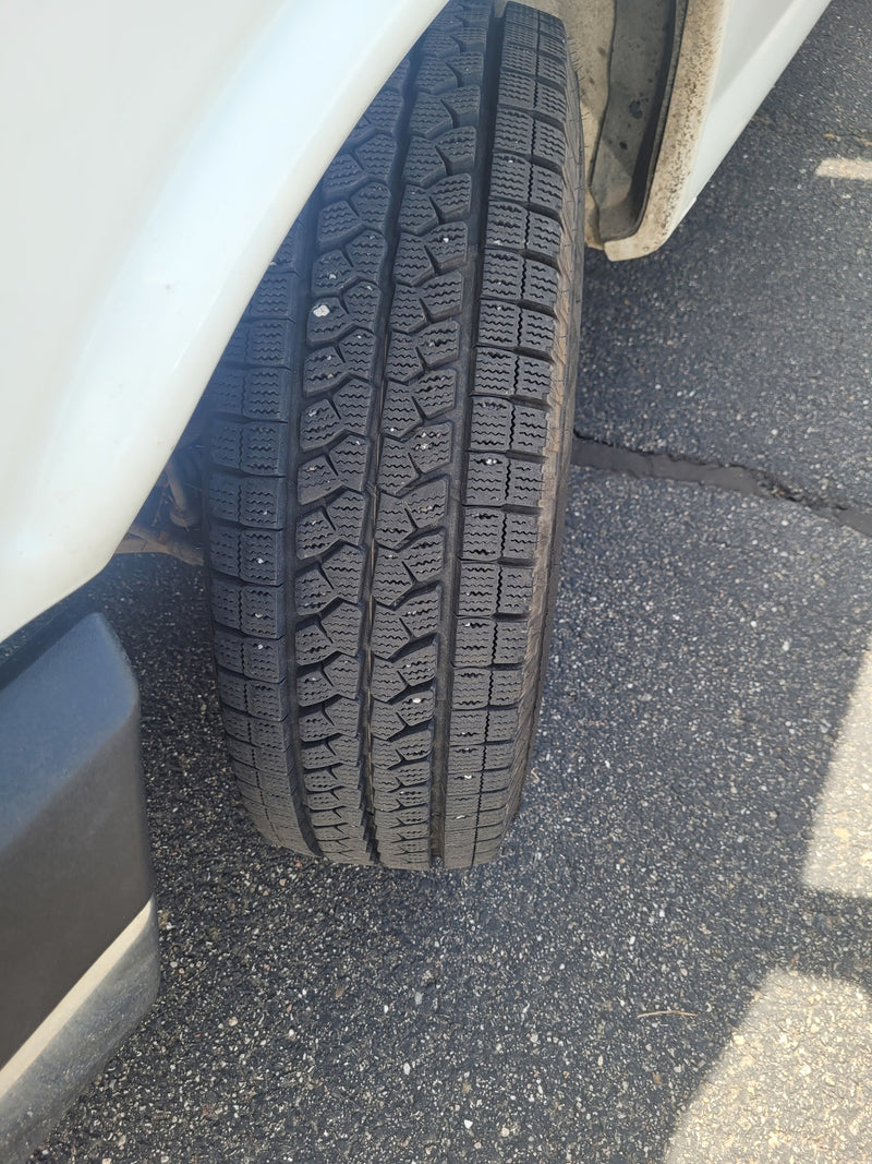 RV rental vehicle's studded winter tire, showcasing its robust tread pattern on asphalt. Ideal for diverse travel conditions. — photo 3