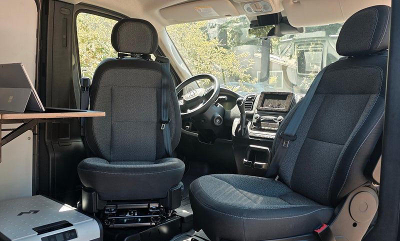 Interior view of an RV rental: front cabin with swiveling seats, a laptop workspace, and cooler for travel comfort. — photo 7