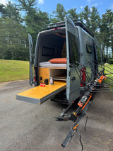 This gray RV rental is a custom camper van with an interior bed, slide-out table, and rear bike rack for outdoor adventures.