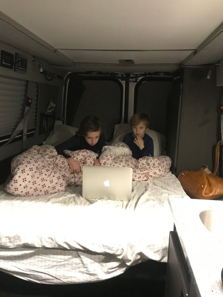 Inside an RV rental, two boys watch a laptop in their bed. A cozy setup for family travel.