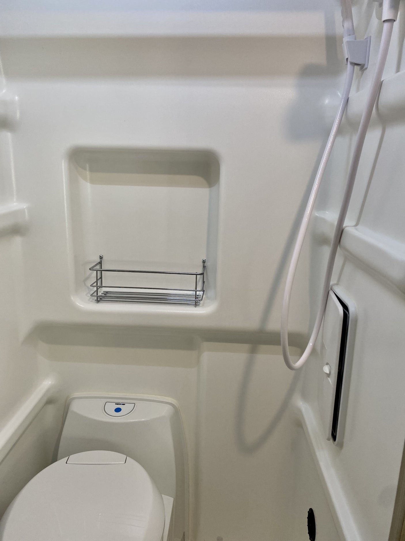 Inside an RV rental: a compact white wet bath featuring a toilet, shower hose, and a practical storage shelf.